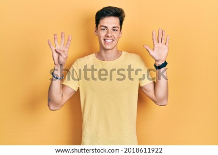 Young hispanic man wearing casual yellow t shirt showing and pointing up with fingers number nine while smiling confident and happy. 