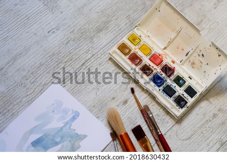 brushes and other watercolor painting tools on white wooden background