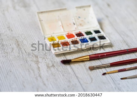brushes and other watercolor painting tools on white wooden background