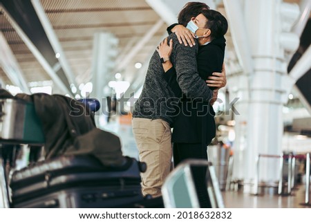 Husband and wife meeting after long separation during covid-19 outbreak at airport arrival gate. Female with face mask welcoming male traveler at airport arrival. Royalty-Free Stock Photo #2018632832