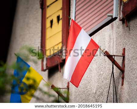 Small flag of Austria on a wall of an old house, cloudy day in springtime