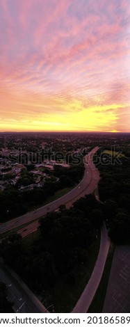 an aerial, vertical panoramic view of a colorful sky and a quiet neighborhood at sunrise. The drone camera is high enough to see the horizon.