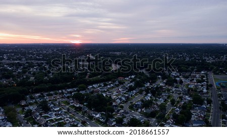 an aerial view of a colorful sky and a quiet suburban neighborhood at sunrise. The drone camera is high enough to see the horizon.