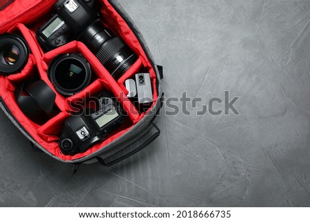 Professional photography equipment in backpack on grey stone table, top view. Space for text