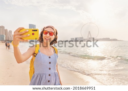 Female travel blogger takes a selfie photo for her social networks against the backdrop of skyscrapers and the famous Ain Ferris Wheel in Dubai