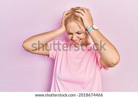 Young blonde woman wearing casual pink t shirt suffering from headache desperate and stressed because pain and migraine. hands on head. 