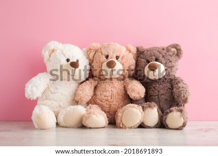 Smiling white, light brown and dark brown teddy bears sitting on table at pink wall background. Pastel color. Togetherness and friendship concept. Front view. Closeup. Royalty-Free Stock Photo #2018691893