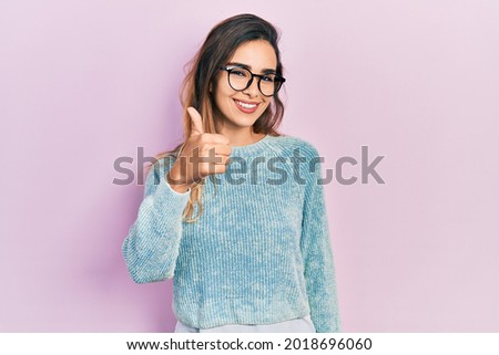 Young hispanic girl wearing casual clothes and glasses smiling happy and positive, thumb up doing excellent and approval sign 