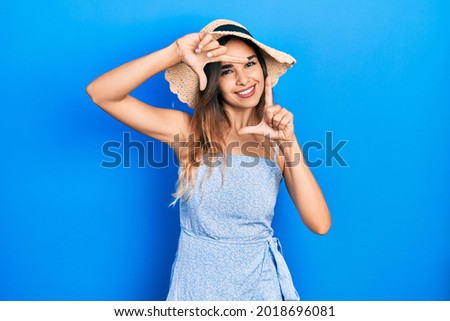 Young hispanic girl wearing summer hat smiling making frame with hands and fingers with happy face. creativity and photography concept. 