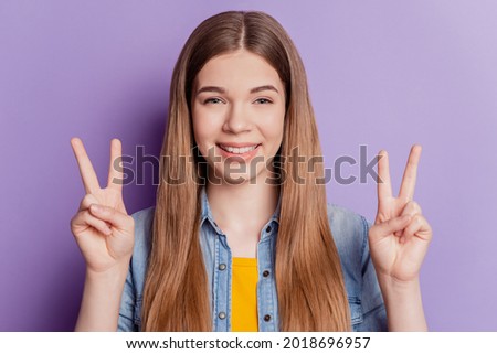 Young woman showing two fingers peace gesture beaming smile on purple background