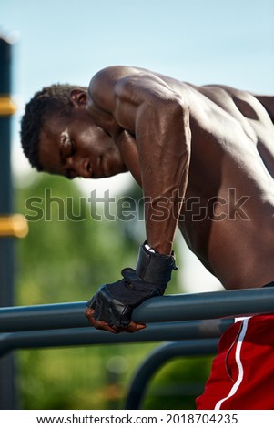Black fitness man exercising on the uneven bars, back shot Cross training of a male model in an urban environment. An African guy in his twenties is training on the street.