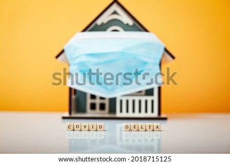 Inscription Covid Delta. Model house in a protective medical mask on a yellow background.