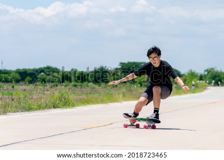 A young Asian man in a black shirt and pants is playing figure skating on a rural road. in the sun on a bright day, Play surf skate
