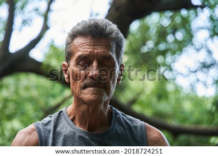 Mature man keeping his eyes closed and enjoying of the nature while meditating