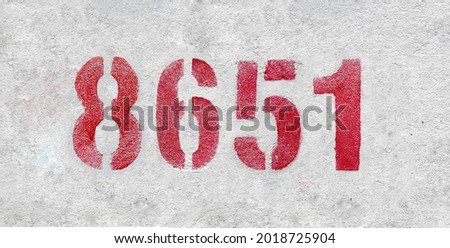 Red Number 8651 on the white wall. Spray paint. Number eight thousand six hundred and fifty one.