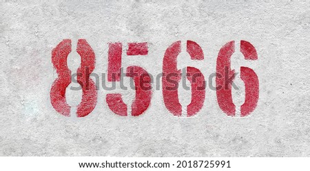 Red Number 8566 on the white wall. Spray paint. Number eight thousand five hundred and sixty six.