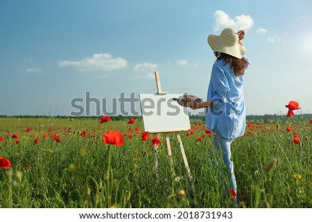 Woman painting on easel in beautiful poppy field