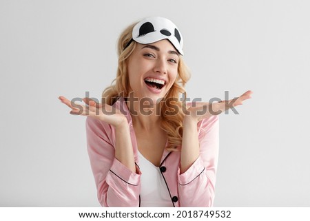 Positive energetic woman enjoying free time in morning at vacation. Portrait of happy millennial pretty blonde female in sleep mask panda laughs and gestures on white wall background, free space