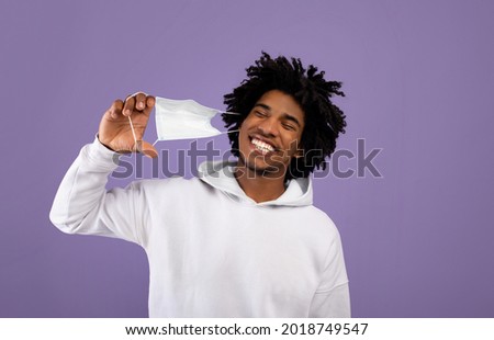 End of coronavirus epidemic. Happy black teenager taking off medical mask, feeling free on violet studio background. African American teen removing facial covid protection, celebrating end of lockdown Royalty-Free Stock Photo #2018749547
