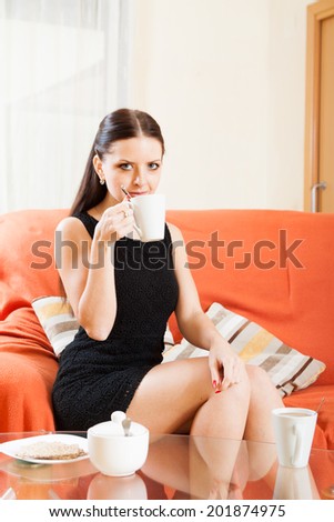  beautiful girl in black dress sitting on  sofa with  cup of tea