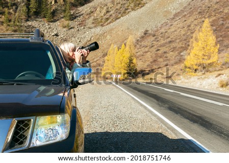 Mature woman taking photo from her car. Woman travel autumn.