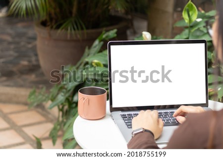 Woman using or typing laptop outside cafe restaurant with natural. Laptop computer on white desk and white blank on screen.