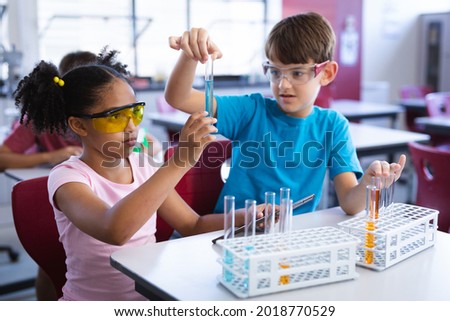 African american girl and caucasian boy holding test tube in science class at elementary school. school and education concept