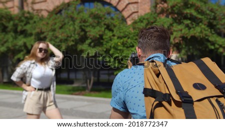 Couple of tourists taking photos with photo camera on historical place in city. Young woman posing in summer city and boyfriend taking photo enjoying romantic trip together