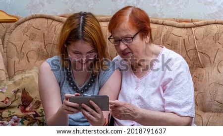 The granddaughter shows her grandmother a photo on her smartphone. A happy family.