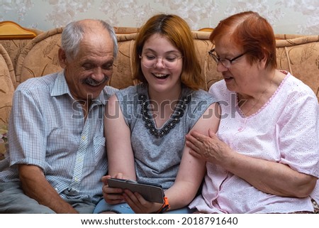 The granddaughter shows her grandparents a photo on a smartphone. A happy family.