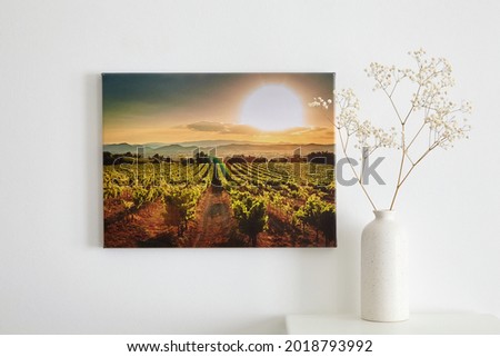 Canvas photo print and flowers in vase, interior decor. Landscape photography hanging on white wall. picture with vineyard