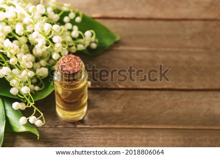 Bottle with essential oil and lily-of-the-valley flowers on wooden background