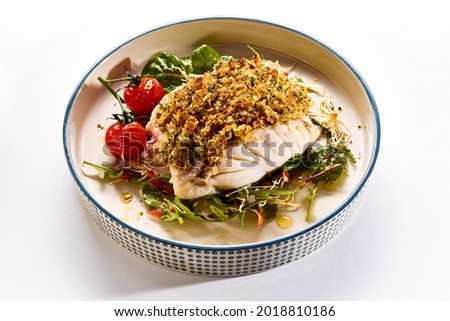 Yummy baked cod fish with breadcrumbs served on ceramic plate with fresh salad leaves and yummy cherry tomatoes