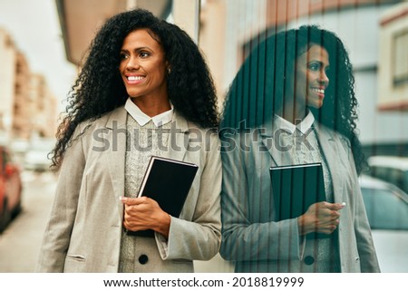 Middle age african american businesswoman smiling happy holding book at the city.