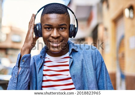 Young african american man smiling happy using headphones at the city.