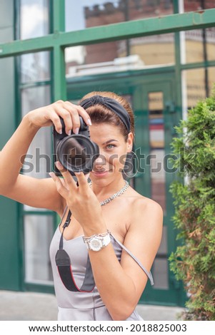A beautiful girl photographer is engaged in shooting the area in the summer, walking around the big city