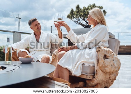 Beautiful mature couple in bathrobes enjoying fruits and wine while relaxing in luxury hotel outdoors Royalty-Free Stock Photo #2018827805