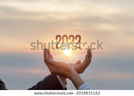 The hands of businessmen show 2022 against the background of a sunny sunset.