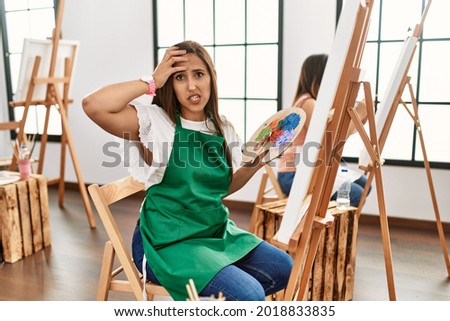 Young hispanic artist women painting on canvas at art studio worried and stressed about a problem with hand on forehead, nervous and anxious for crisis 