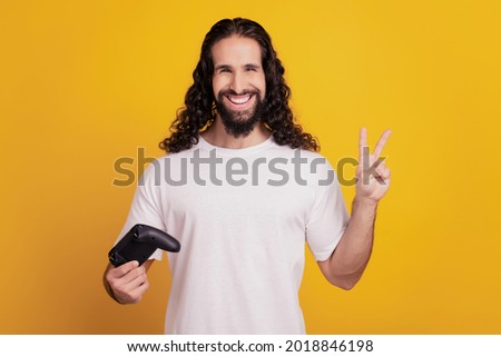 Portrait of friendly player guy hold gamepad show v-sign on yellow background