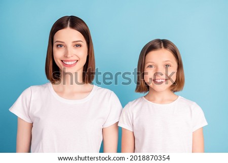 Photo of two pretty charming sisters wear white t-shirts smiling isolated blue color background
