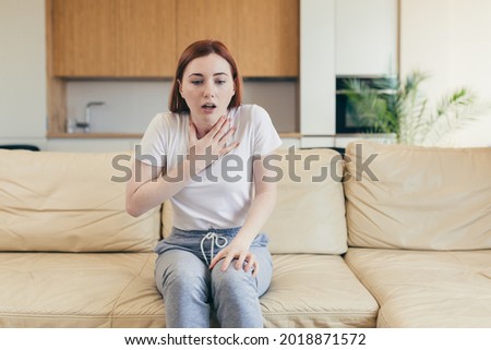 Young woman alone at home with a panic attack shortness of breath, trembling, numbness, loss of consciousness. Front view of a female suffering an anxiety sitting on a couch. chest pain, fear symptom Royalty-Free Stock Photo #2018871572