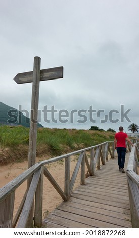 man walking along signposted wooden walkway on cloudy autumn day
