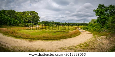 Curved dirt road in the wooded green field. Dramatic clouds and tranquil agricultural meadow on Cape Cod.