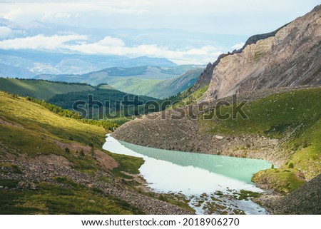 Colorful green landscape with beautiful turquoise mountain lake in sunlight. Impressive scenery with turquoise lake on background of green mountains with forest and low clouds. Scenic mountains view.
