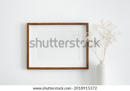 Landscape wooden frame mockup with copy space for artwork, photo or print presentation. White wall and vase with dry gypsophila flower decoration.