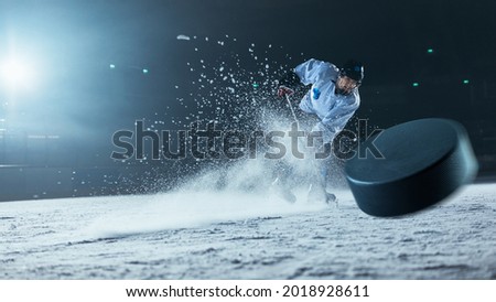Ice Hockey Rink Arena: Professional Player Shooting the Puck with Hockey Stick. Focus on 3D Flying Puck with Blur Motion Effect. Dramatic Wide Shot, Cinematic Lighting. Royalty-Free Stock Photo #2018928611