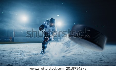 Ice Hockey Rink Arena: Professional Player Shooting the Puck with Hockey Stick. Focus on 3D Flying Puck with Blur Motion Effect. Dramatic Wide Shot, Cinematic Lighting. Royalty-Free Stock Photo #2018934275