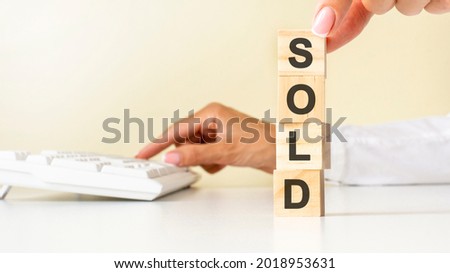 Close up young woman's hand in white shirt wooden block cube for SOLD wording on white table floor, white keyboard on the background. financial and business concepts