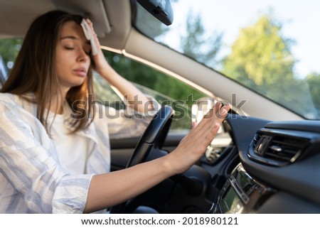 Woman driver has problem with a non-working conditioner, hand checking flow cold air, being hot during heat wave in car, suffering from summer hot weather, wipes sweat from her forehead with tissue.  Royalty-Free Stock Photo #2018980121